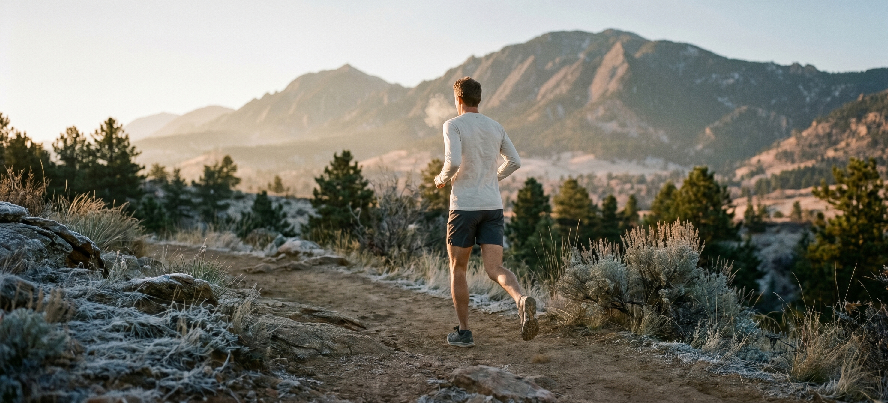 A runner at dawn on a Boulder trail, breath visible, mid-stride.